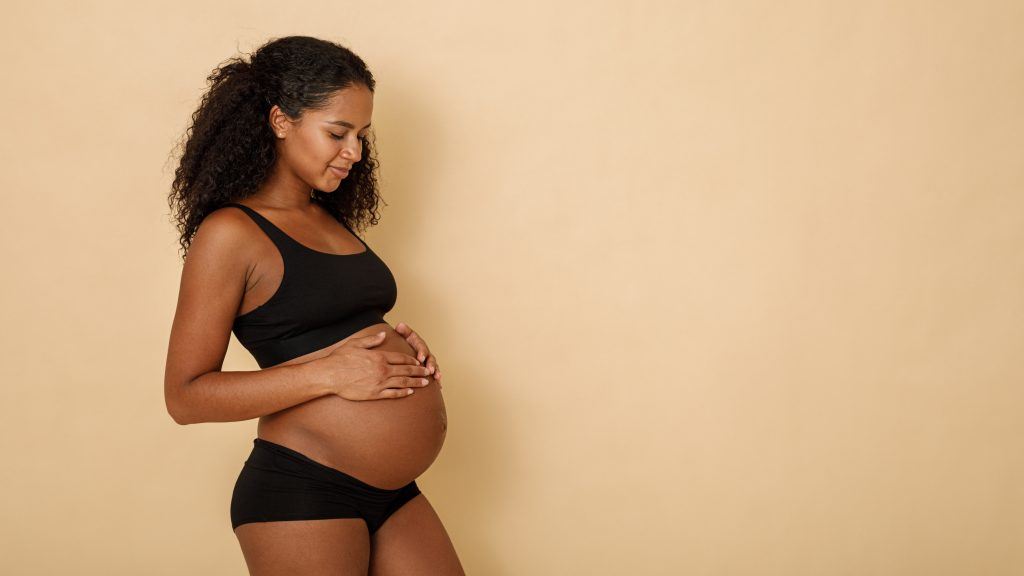 Studio shot of a pregnant woman looking on her belly, copy space