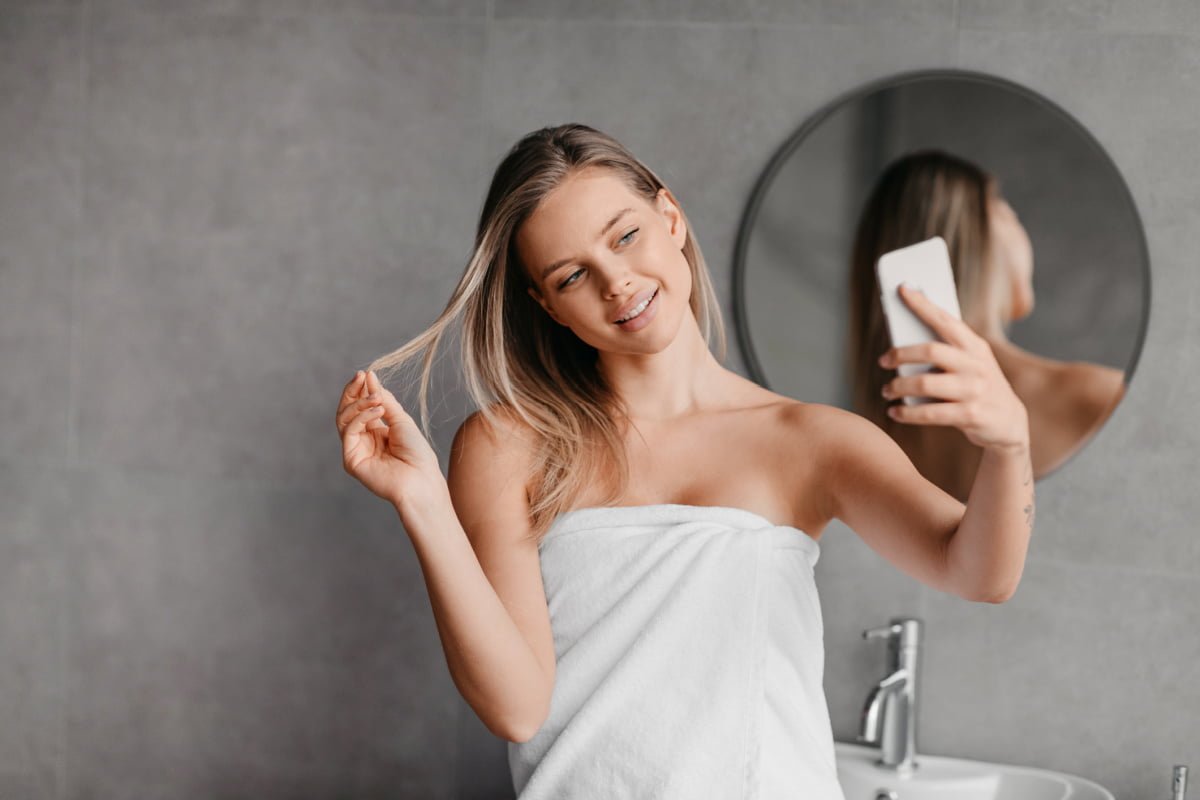 Young woman looking at phone in mirror
