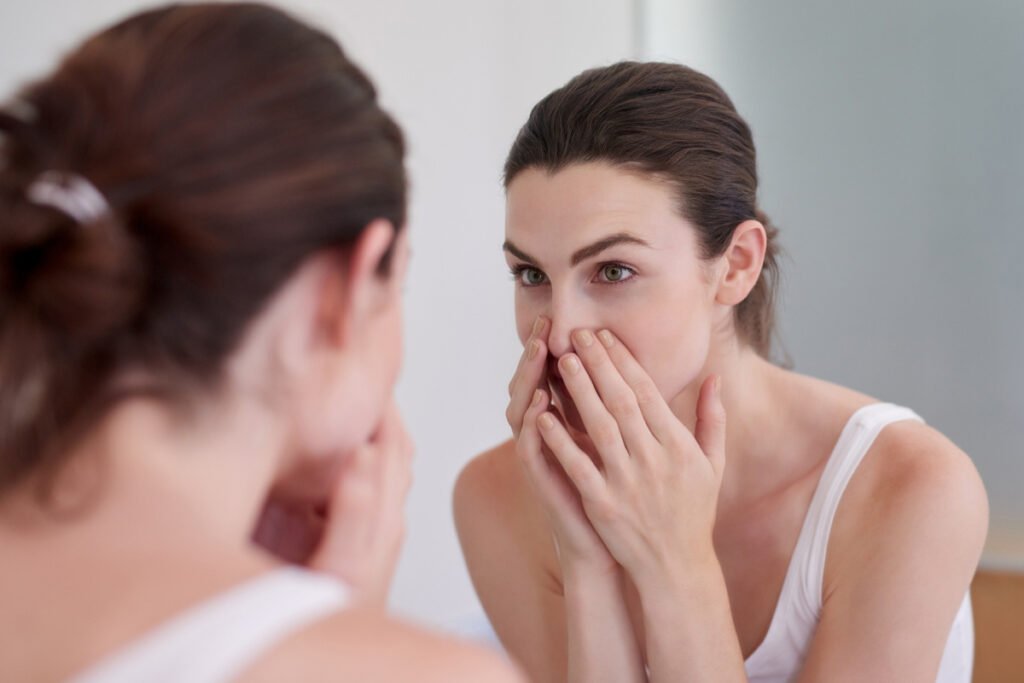 Woman touching nose in mirror before nose reshaping surgery